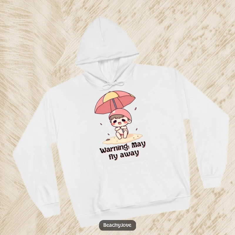 Funny hoodie showing a kawaii character being tumbled by a beach umbrella, looking flustered on a sandy beach, warm and cozy.